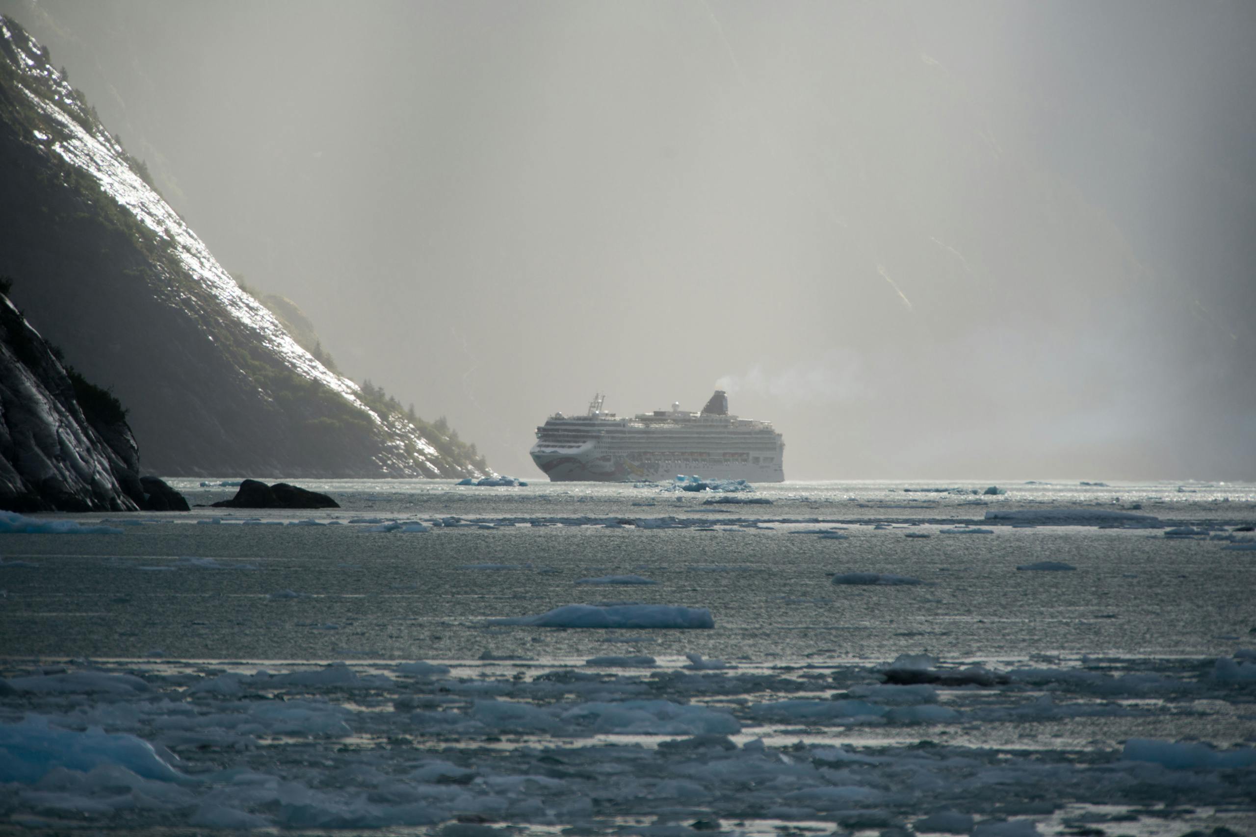 A cruise ship sails through icy Alaskan waters near Juneau under a misty gray sky.