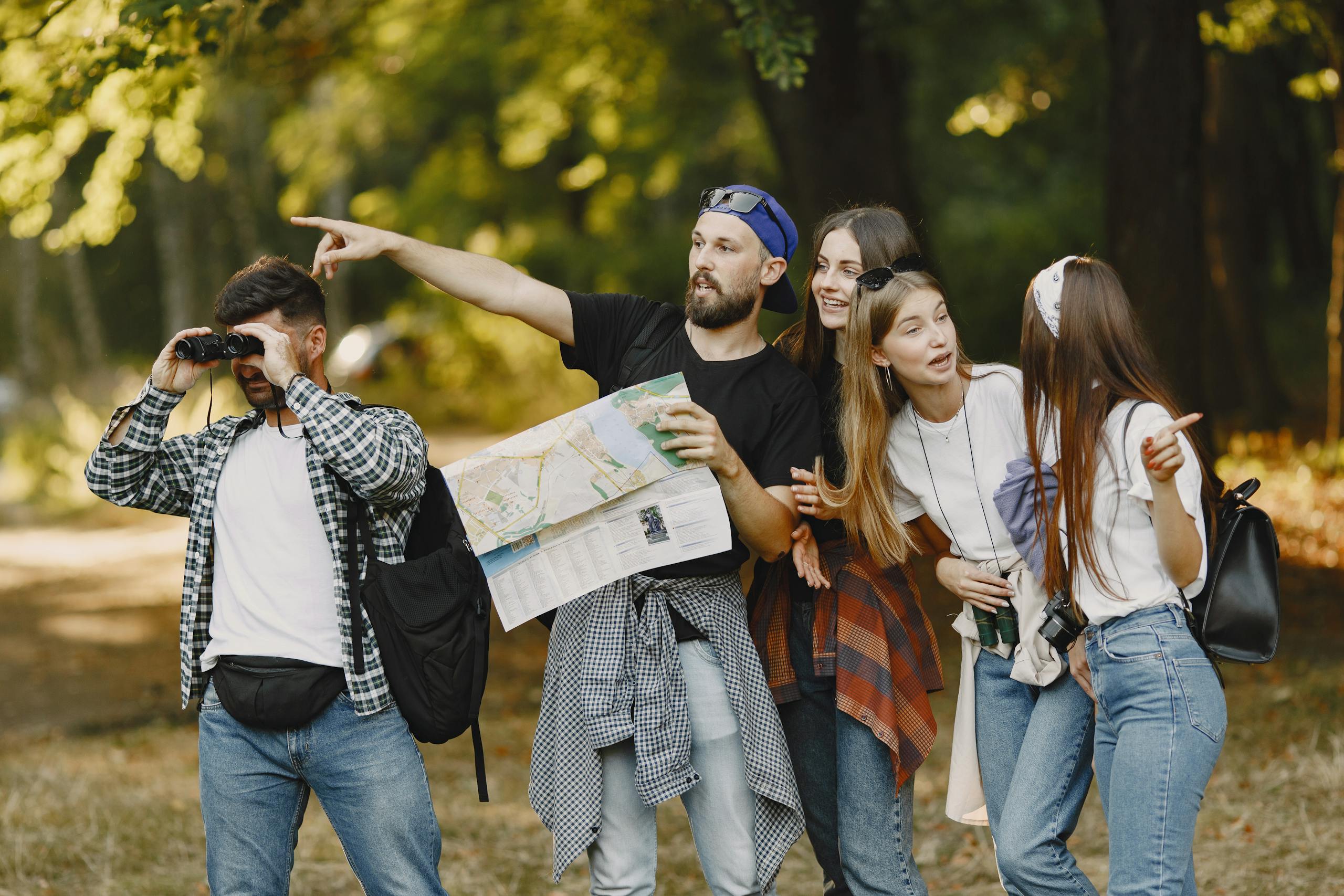 Group of friends navigating nature with map and binoculars, enjoying a summer hike.
