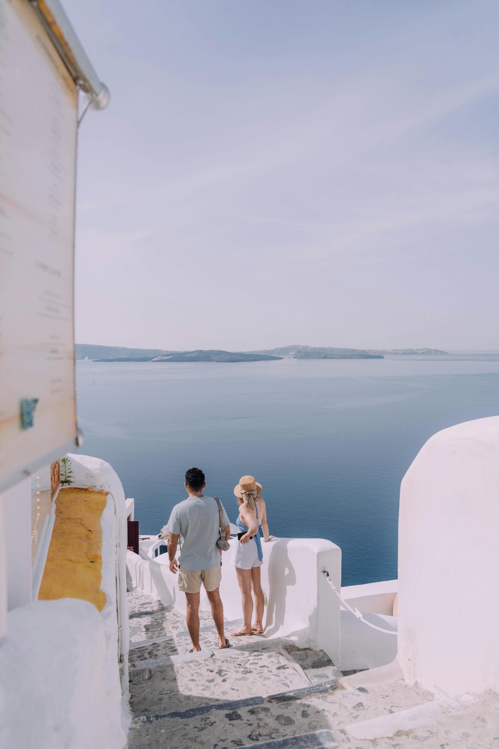 Two people walking down a stone staircase overlooking the sea in Santorini, Greece.