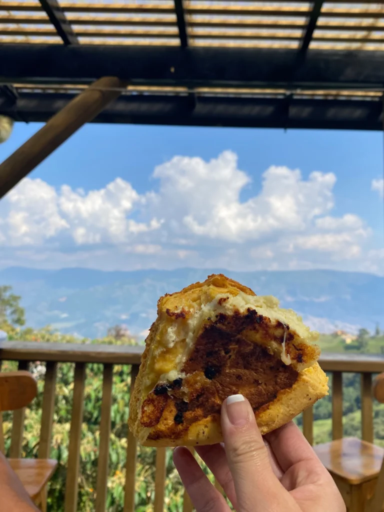 Freshly grilled Panchoca cheese bread held up against a mountain view in San Félix near Medellín