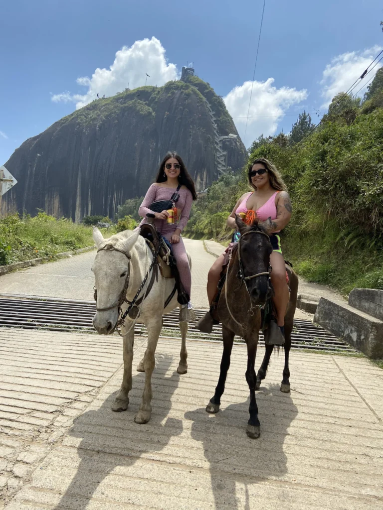 Two travelers on horseback in front of the El Peñol rock in Guatapé near Medellín, Colombia
