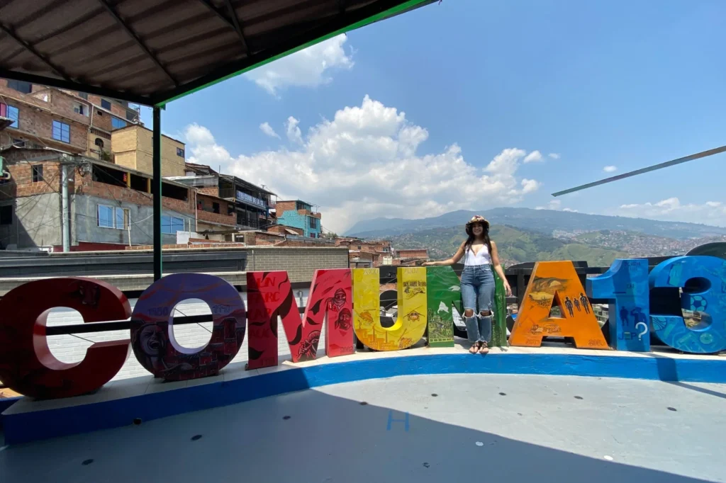Traveler standing beside the colorful COMUNA 13 letter sculpture overlooking the neighborhood in Medellín